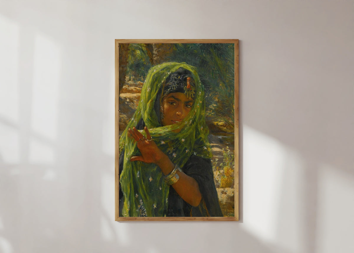 Framed art print of The Girl in the Green Scarf by Nasreddine Dinet, in a light wood frame on a sunlit white wall