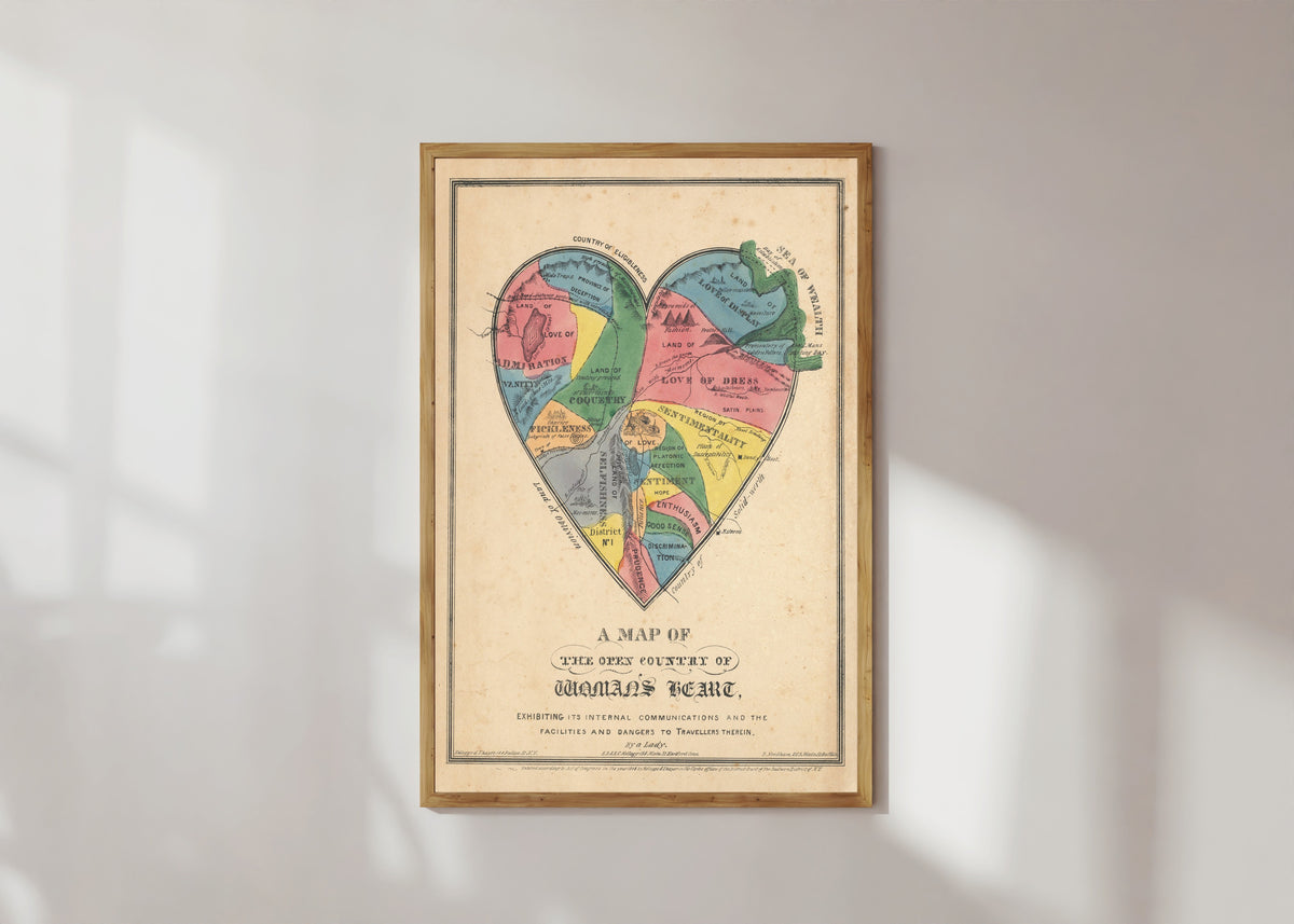 Framed art print of A Map of the Open Country of Woman's Heart by E.B. & E.C. Kellogg, in a light wood frame on a sunlit white wall