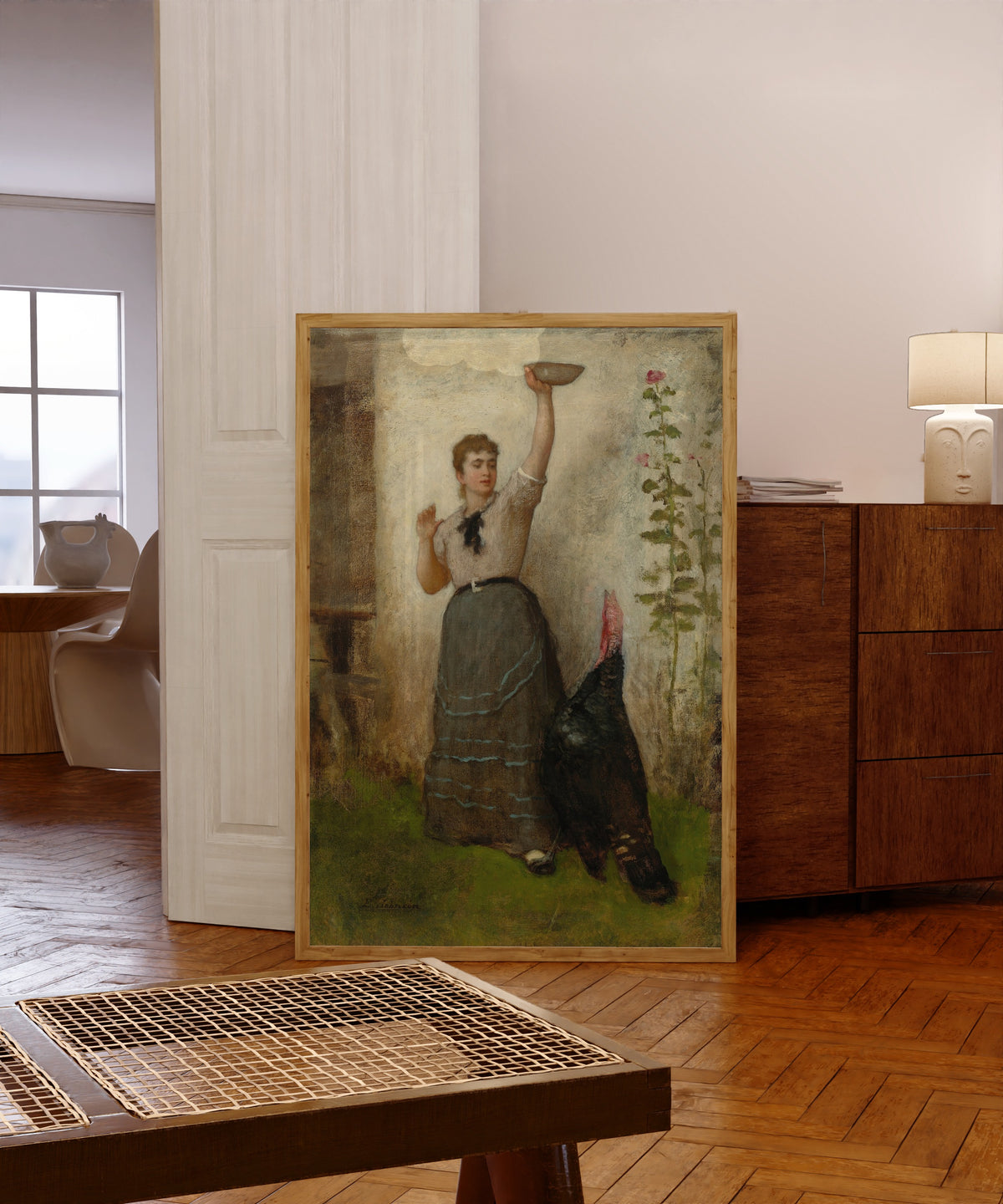 Framed art print of Feeding the Turkey by Eastman Johnson, in a light wood frame leaning in a warm room with a parquet floor