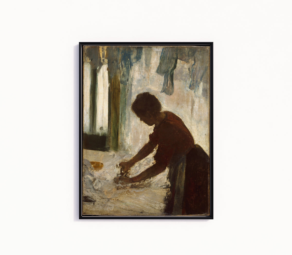 Framed art print of A Woman Ironing by Edgar Degas, in a slim black frame on a plain white wall