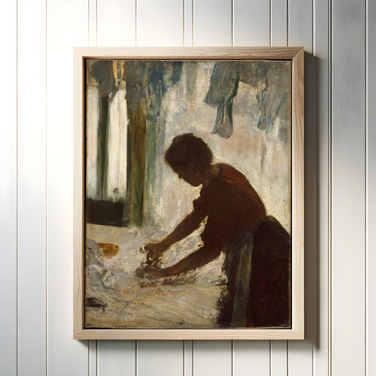 Framed art print of A Woman Ironing by Edgar Degas, in a light wood frame on a white panelled wall