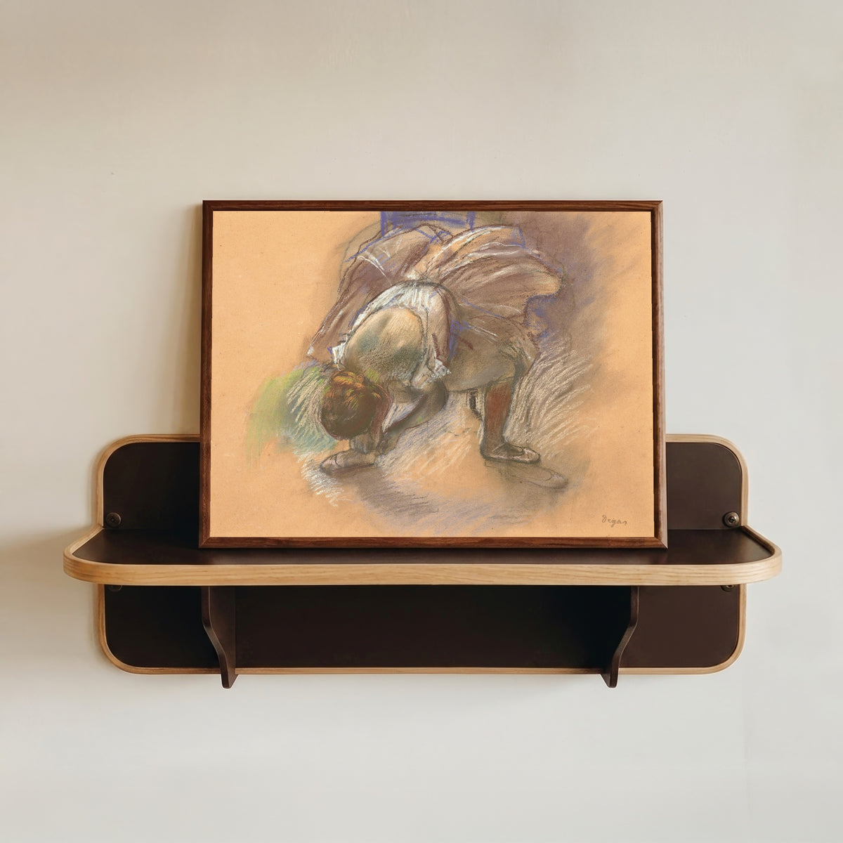 Framed art print of Dancer Adjusting Her Slipper (Lilac Tutu) by Edgar Degas, in a dark wood frame resting on a wall shelf
