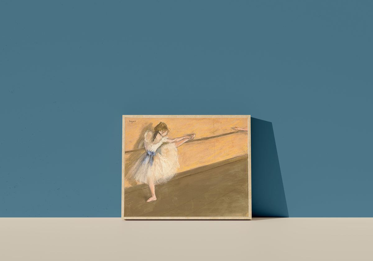 Framed art print of Dancer at the Barre (Orange Wall) by Edgar Degas, in a light wood frame leaning on a blue wall