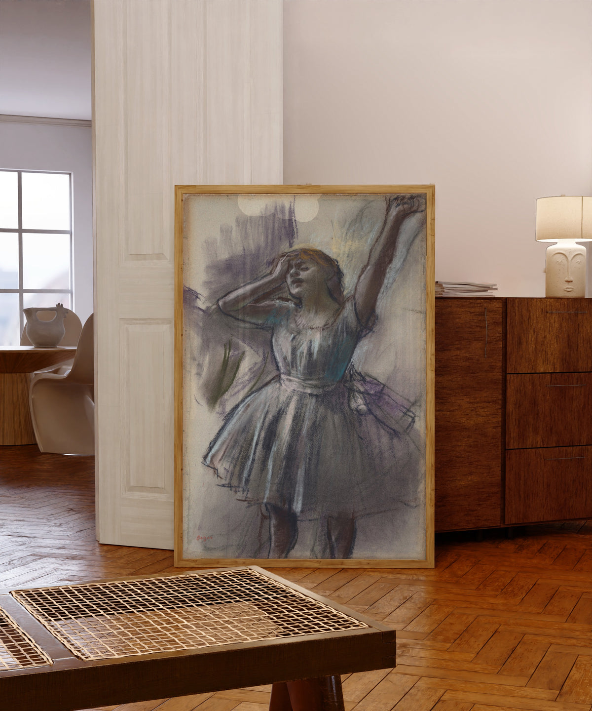Framed art print of Dancer Stretching by Edgar Degas, in a light wood frame leaning in a warm room with a parquet floor