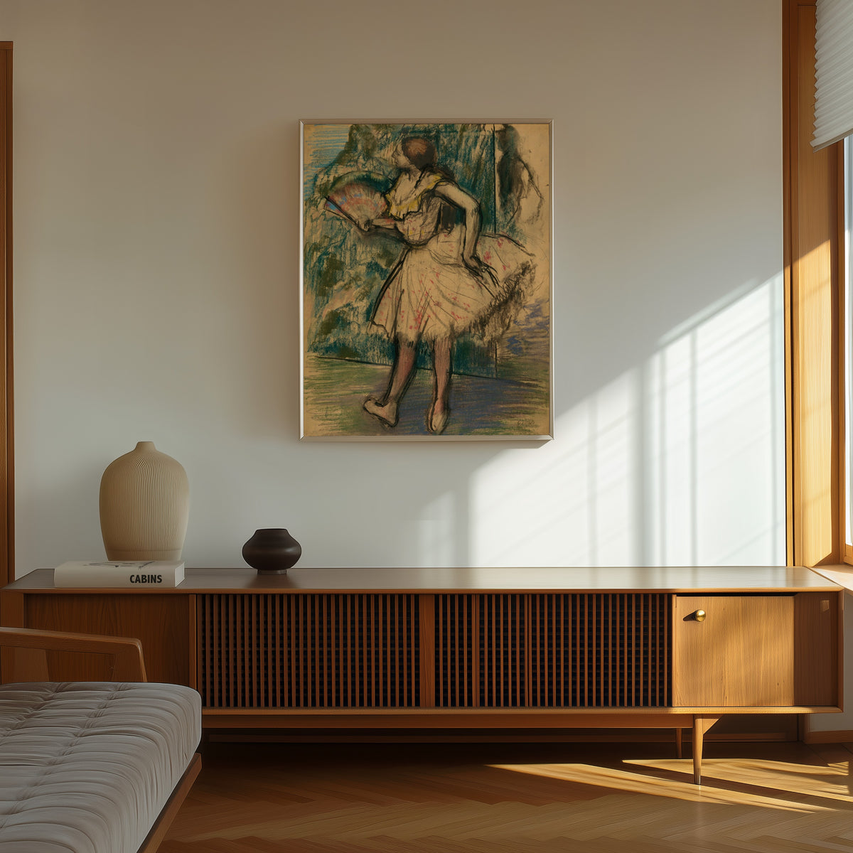 Framed art print of Dancer with a Fan by Edgar Degas, in a thin light frame on a sunlit wall above a wooden sideboard