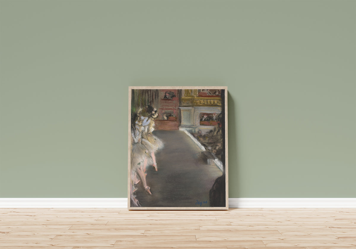 Framed art print of Dancers at the Old Opera House by Edgar Degas, in a light wood frame leaning on a sage green wall above a wooden floor