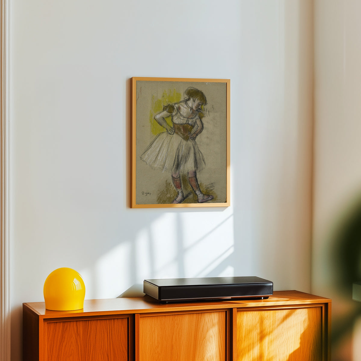 Framed art print of Danseuse (Hands on Hips) by Edgar Degas, in a light wood frame on a white wall above an orange sideboard