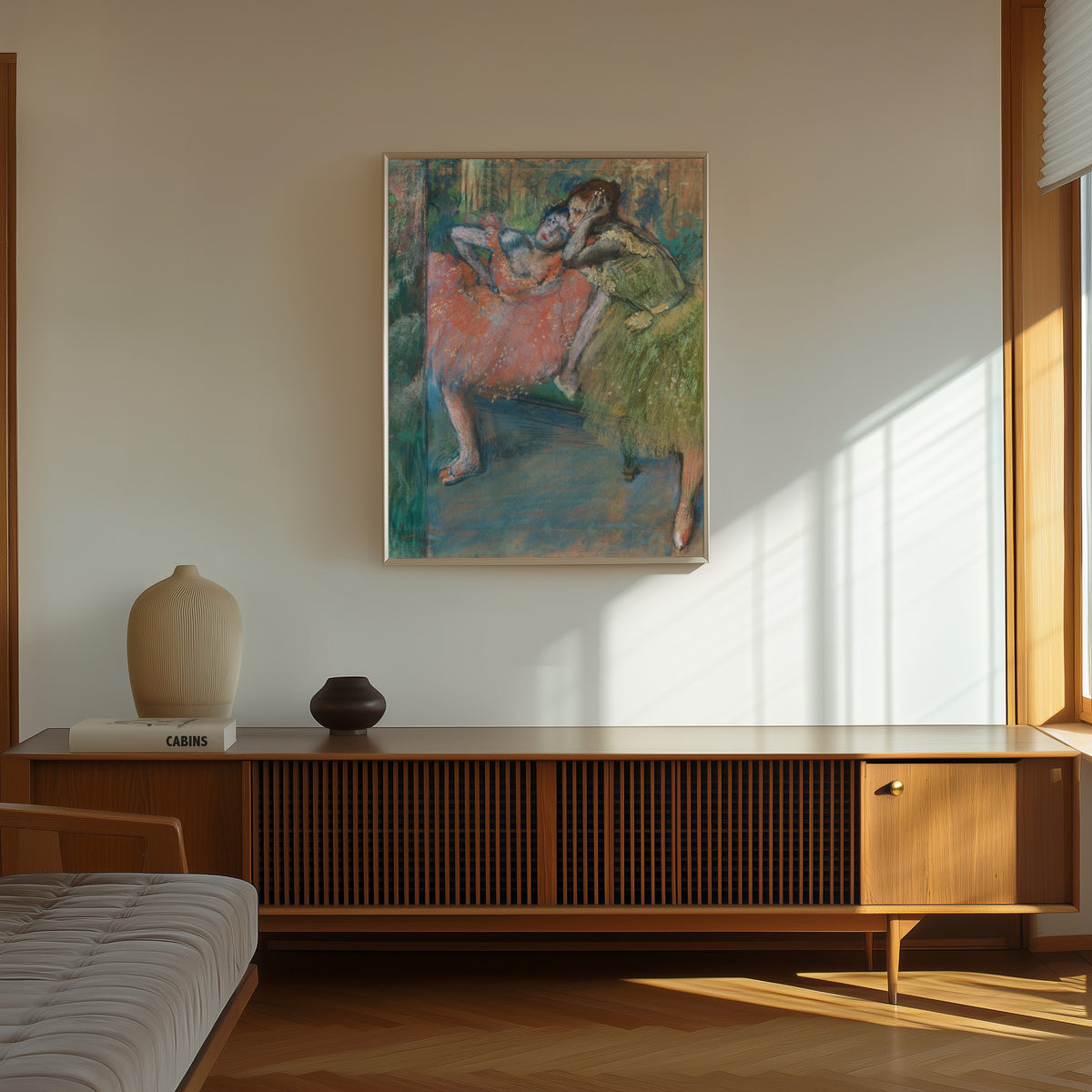 Framed art print of Danseuses au foyer by Edgar Degas, in a thin light frame on a sunlit wall above a wooden sideboard