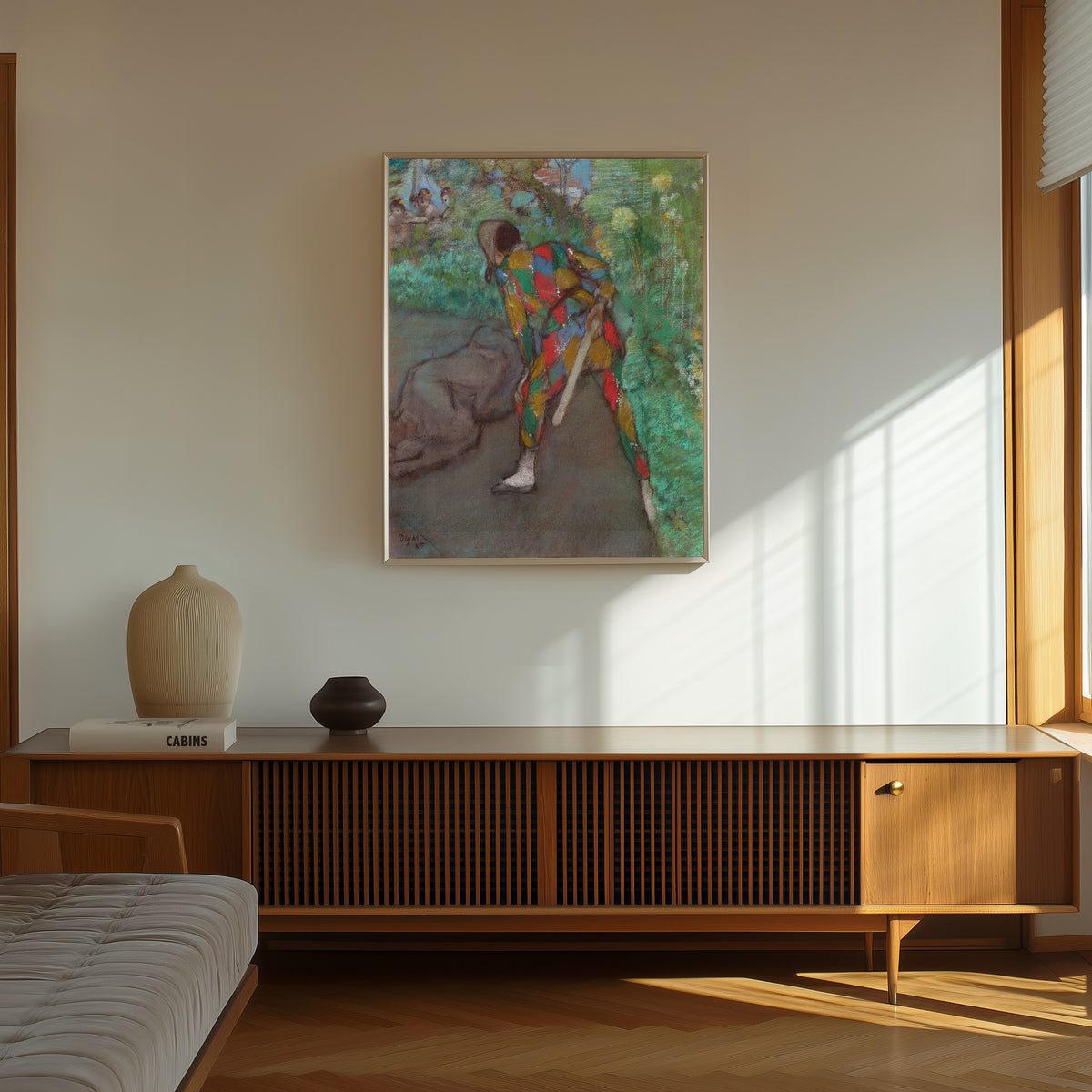 Framed art print of Harlequin by Edgar Degas, in a thin light frame on a sunlit wall above a wooden sideboard