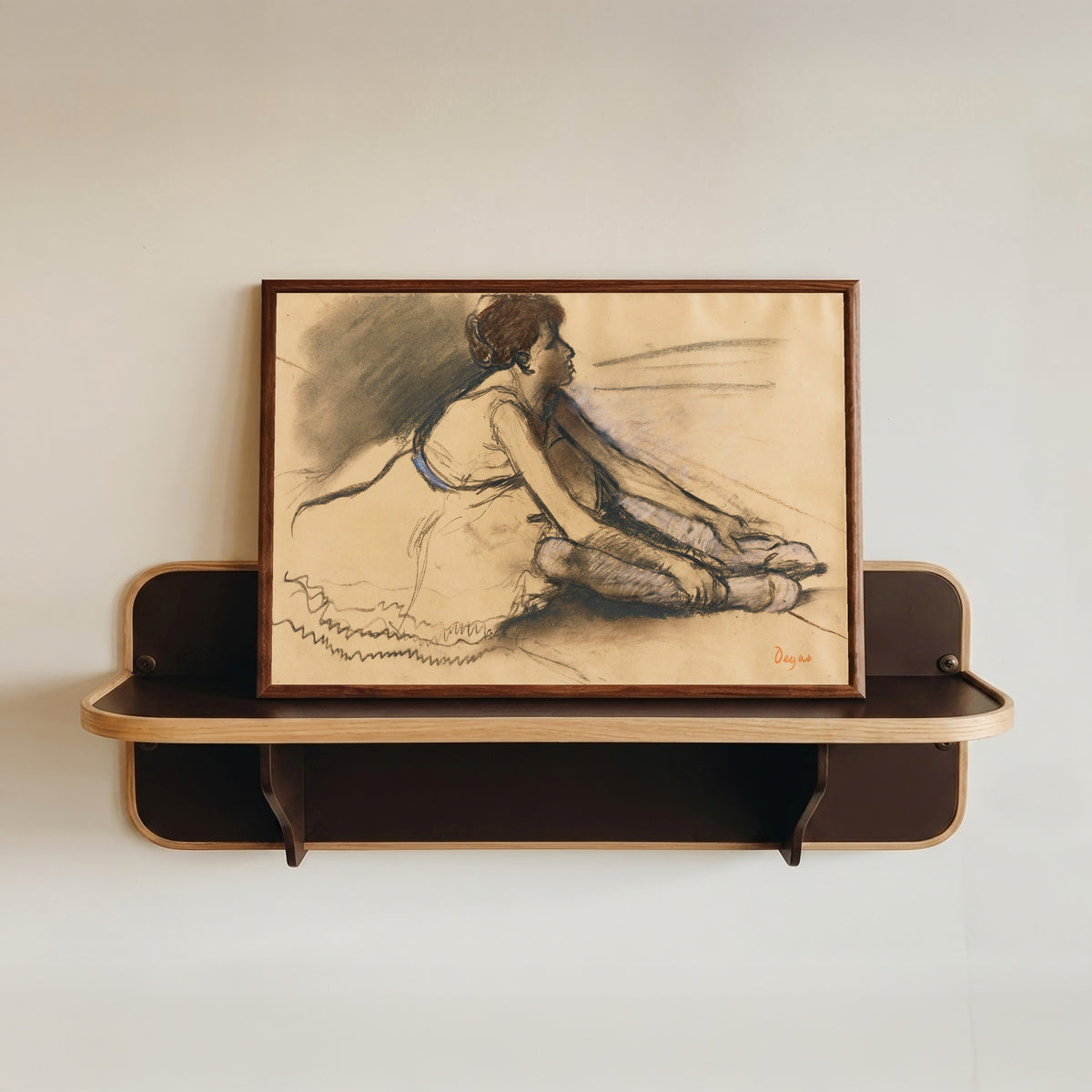 Framed art print of Le repos de la danseuse by Edgar Degas, in a dark wood frame resting on a wall shelf