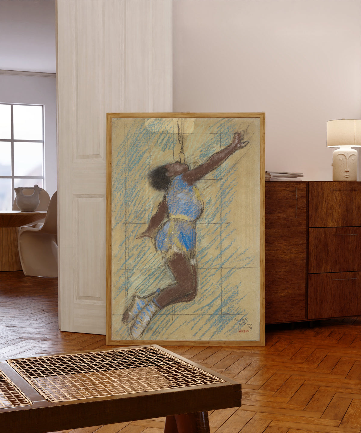 Framed art print of Miss Lala at the Fernando Circus by Edgar Degas, in a light wood frame leaning in a warm room with a parquet floor
