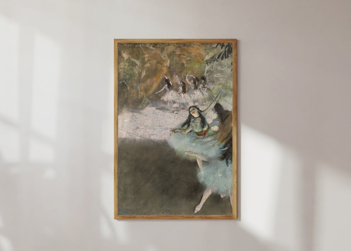Framed art print of On the Stage by Edgar Degas, in a light wood frame on a sunlit white wall