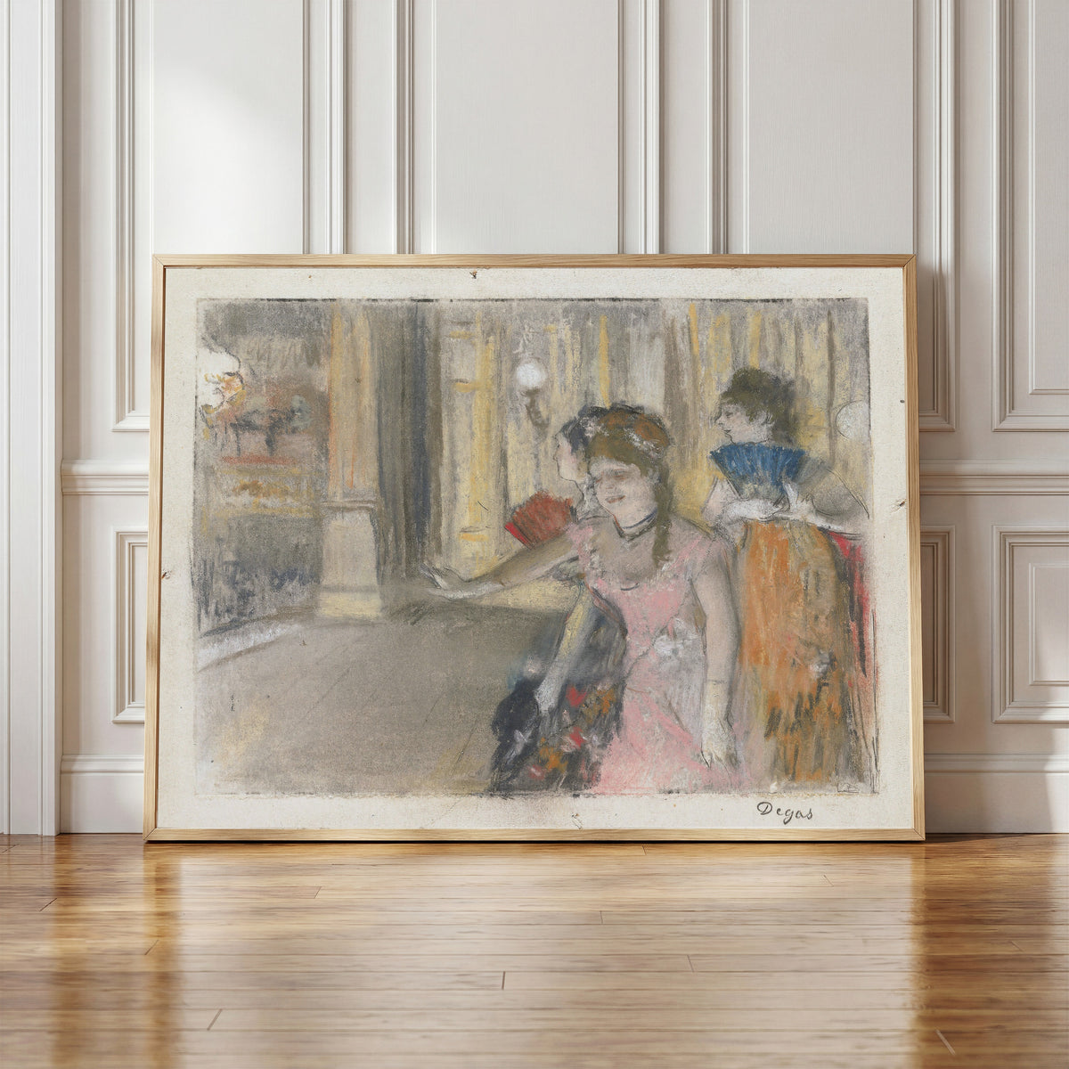 Framed art print of Singers on the Stage by Edgar Degas, in a light wood frame leaning against a panelled white wall