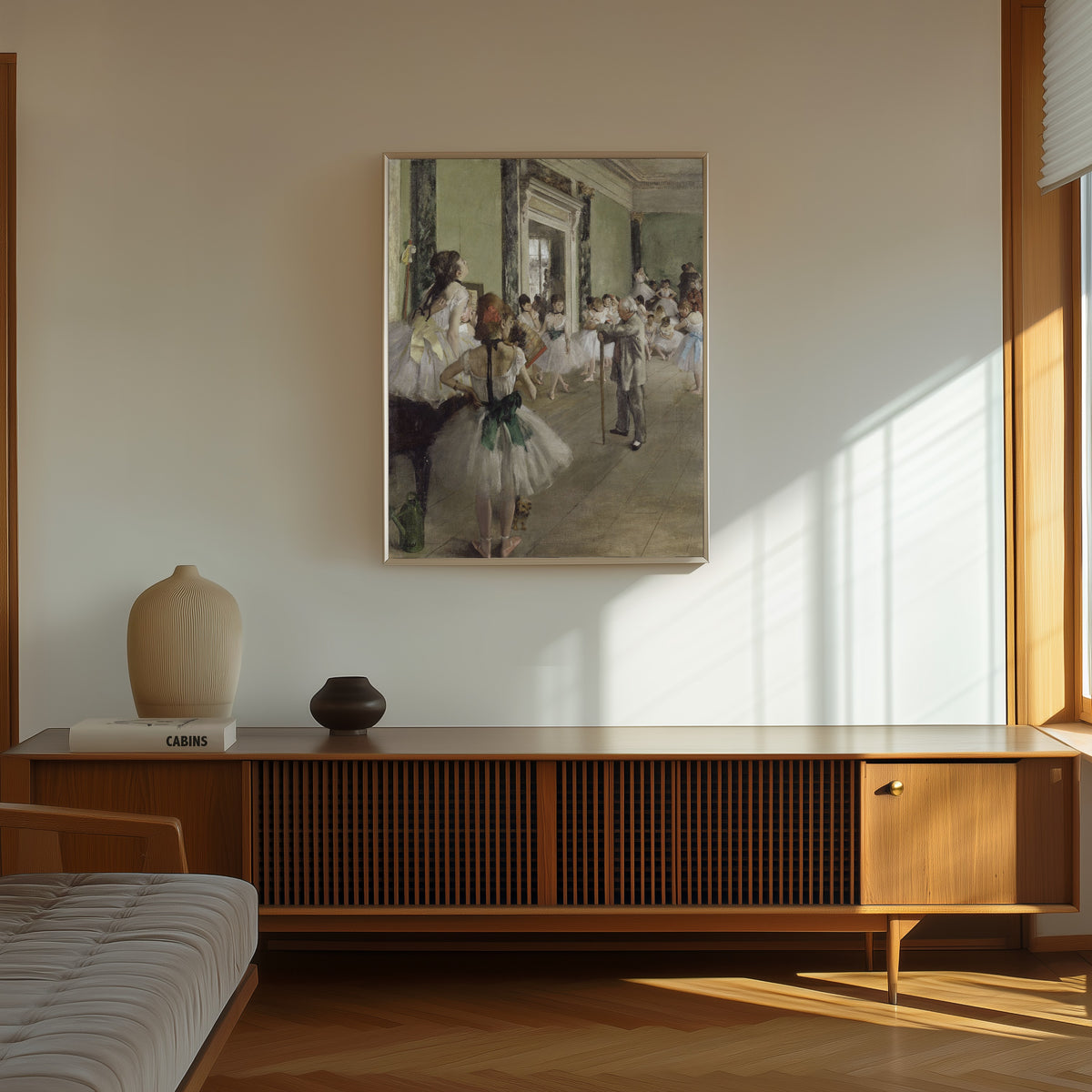 Framed art print of The Ballet Class by Edgar Degas, in a thin light frame on a sunlit wall above a wooden sideboard
