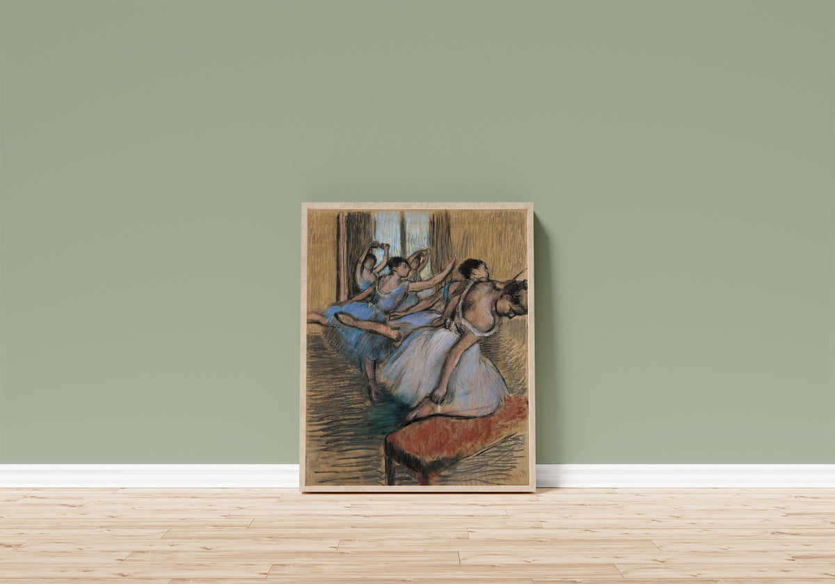 Framed art print of The Dancers (Red Bench) by Edgar Degas, in a light wood frame leaning on a sage green wall above a wooden floor