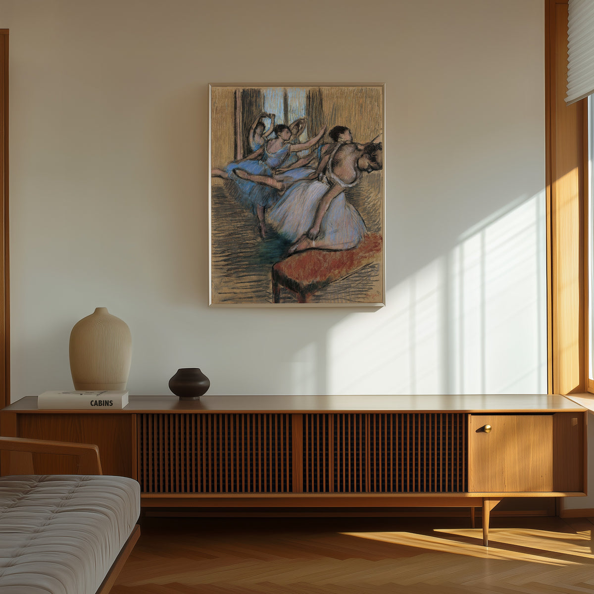 Framed art print of The Dancers (Red Bench) by Edgar Degas, in a thin light frame on a sunlit wall above a wooden sideboard