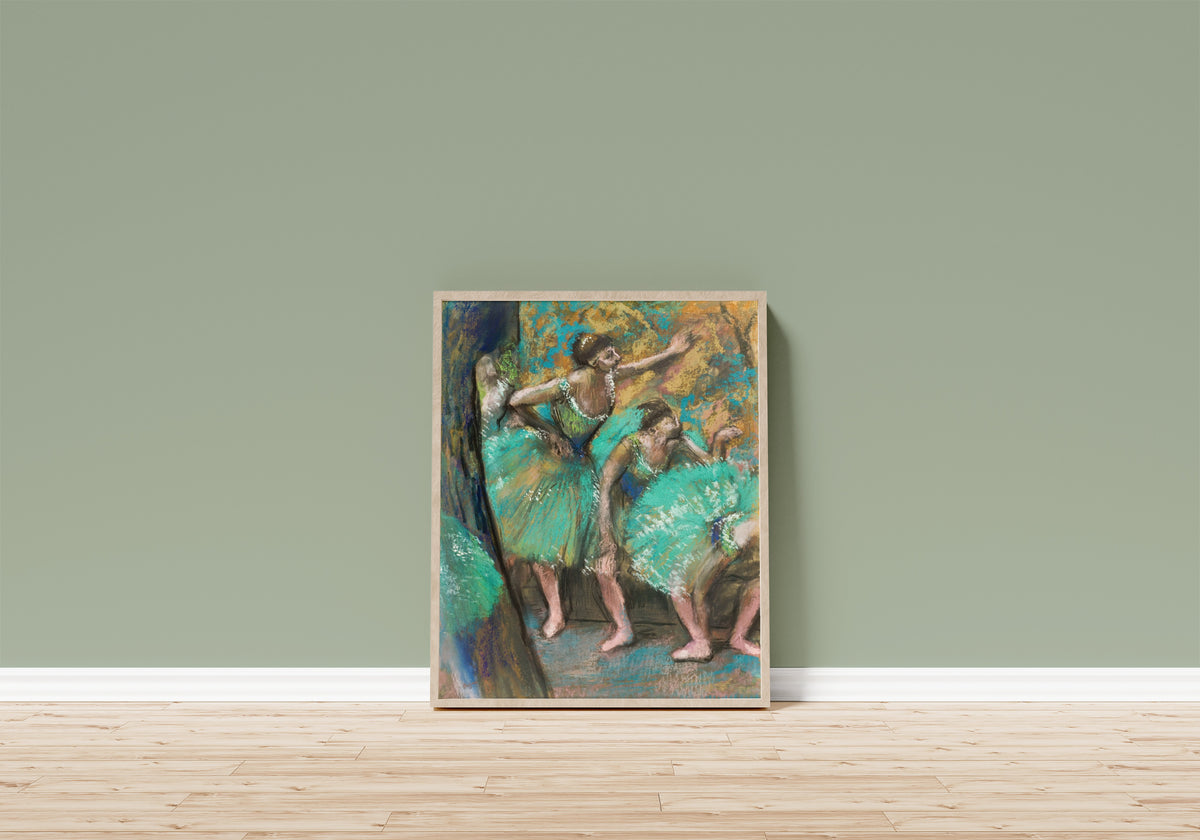 Framed art print of The Dancers (Turquoise Skirts) by Edgar Degas, in a light wood frame leaning on a sage green wall above a wooden floor