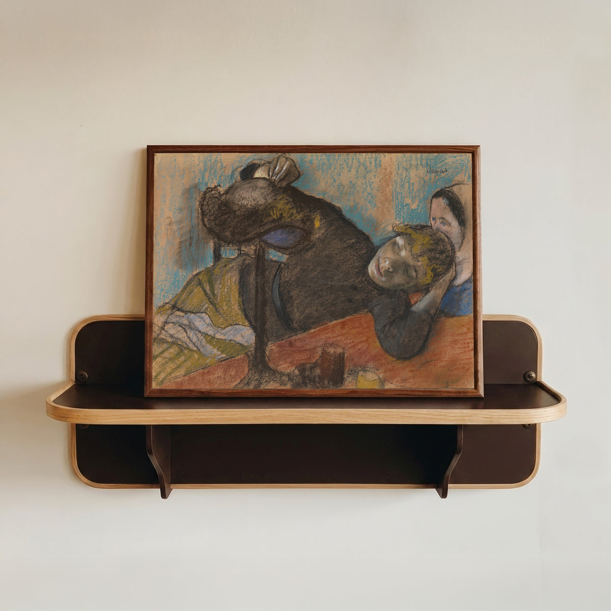 Framed art print of The Milliner by Edgar Degas, in a dark wood frame resting on a wall shelf