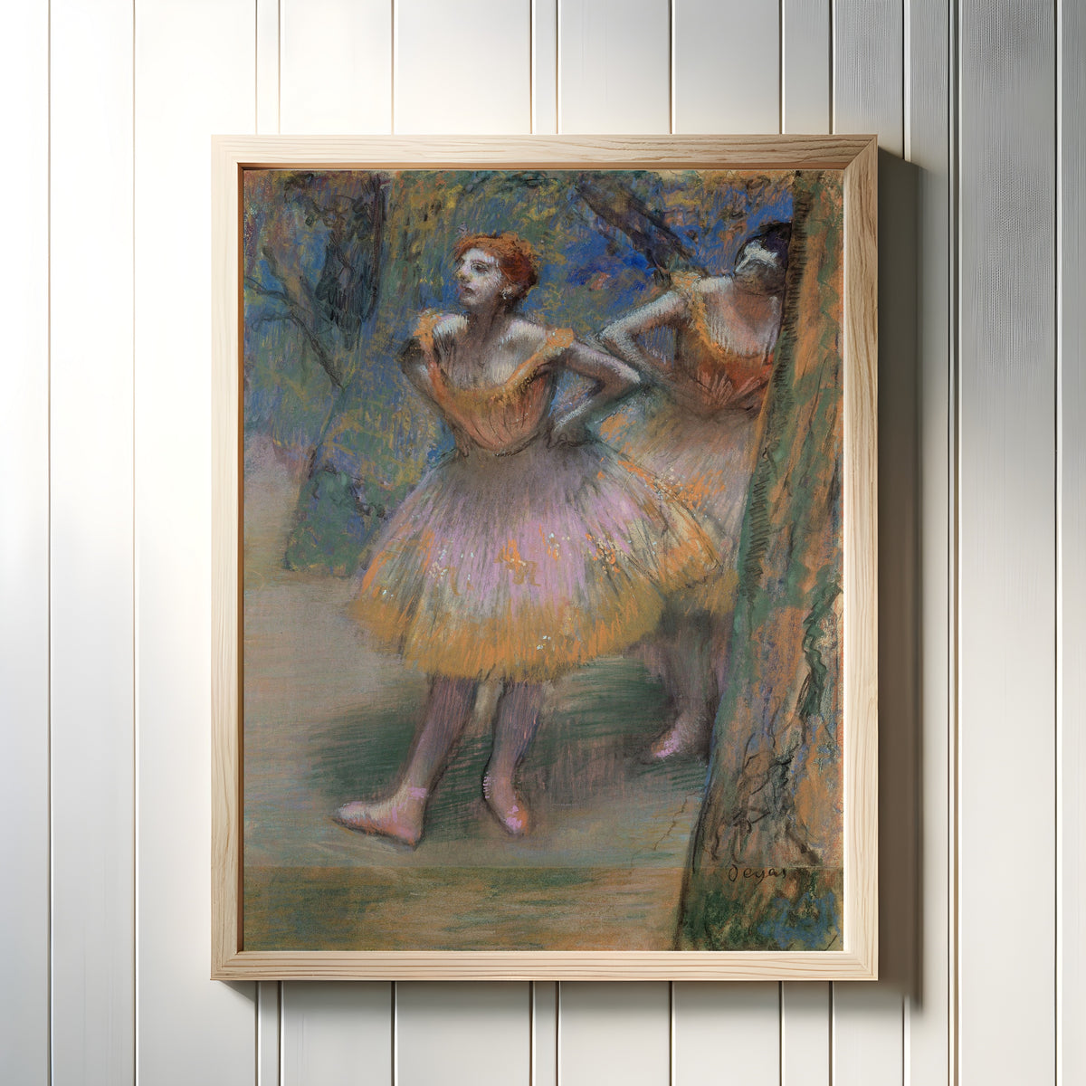 Framed art print of Two Dancers (Lilac and Orange Tutus) by Edgar Degas, in a light wood frame on a white panelled wall