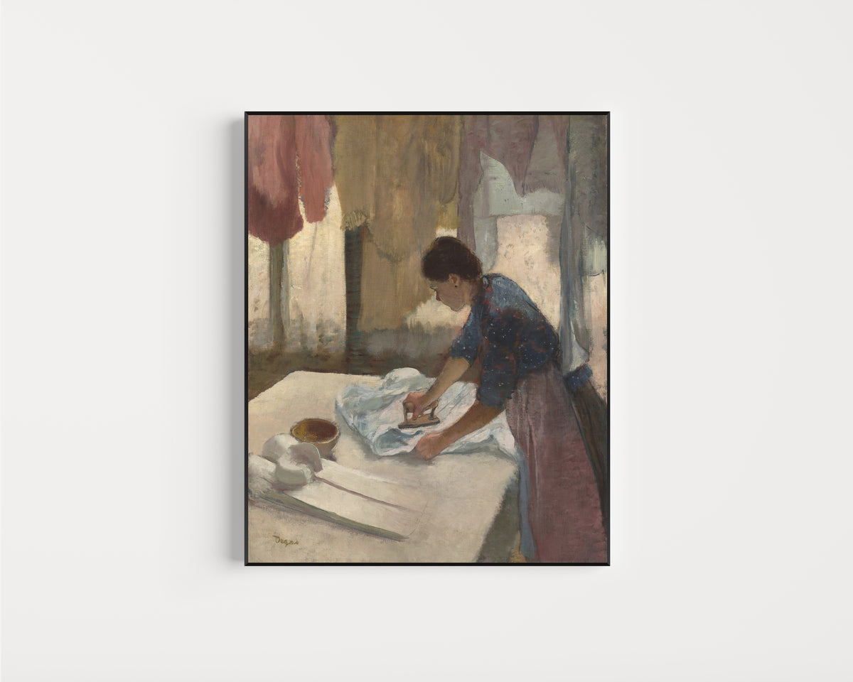 Framed art print of Woman Ironing in a Blue Blouse by Edgar Degas, in a slim black frame on a plain white wall