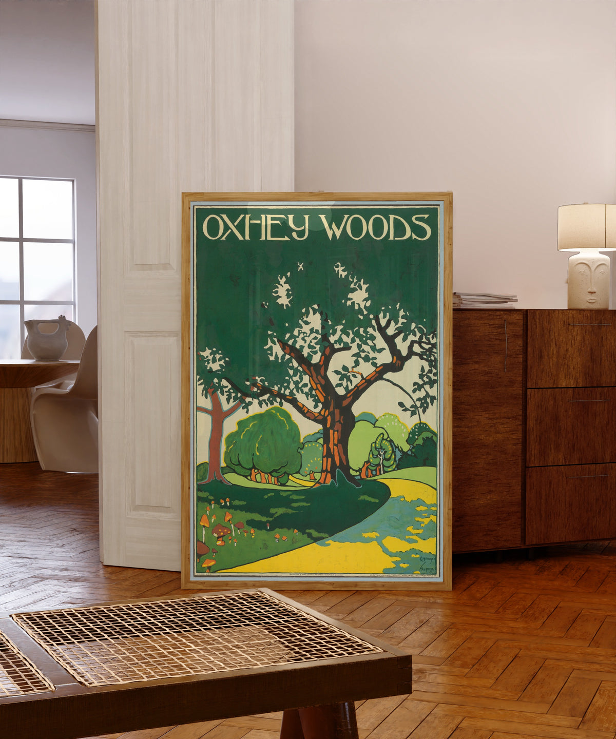 Framed art print of Oxhey Woods by Edward McKnight Kauffer, in a light wood frame leaning in a warm room with a parquet floor