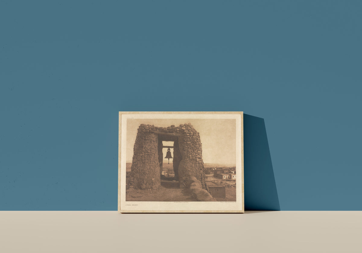 Framed art print of Acoma Belfry by Edward S. Curtis, in a light wood frame leaning on a blue wall