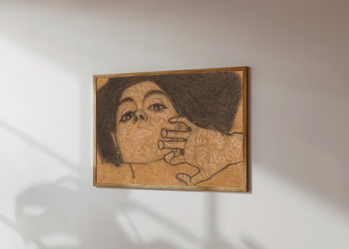 Framed art print of Head of a Woman by Egon Schiele, in a light wood frame on a sunlit white wall, seen at a slight angle