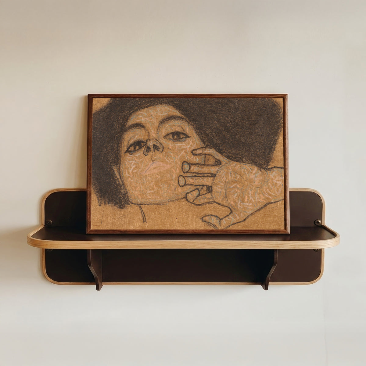 Framed art print of Head of a Woman by Egon Schiele, in a dark wood frame resting on a wall shelf