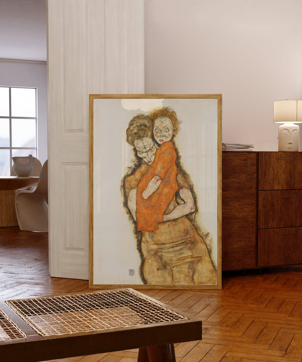 Framed art print of Mother and Child by Egon Schiele, in a light wood frame leaning in a warm room with a parquet floor