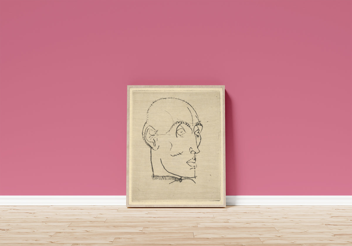Framed art print of Portrait of a Man by Egon Schiele, in a light wood frame leaning on a pink wall above a wooden floor
