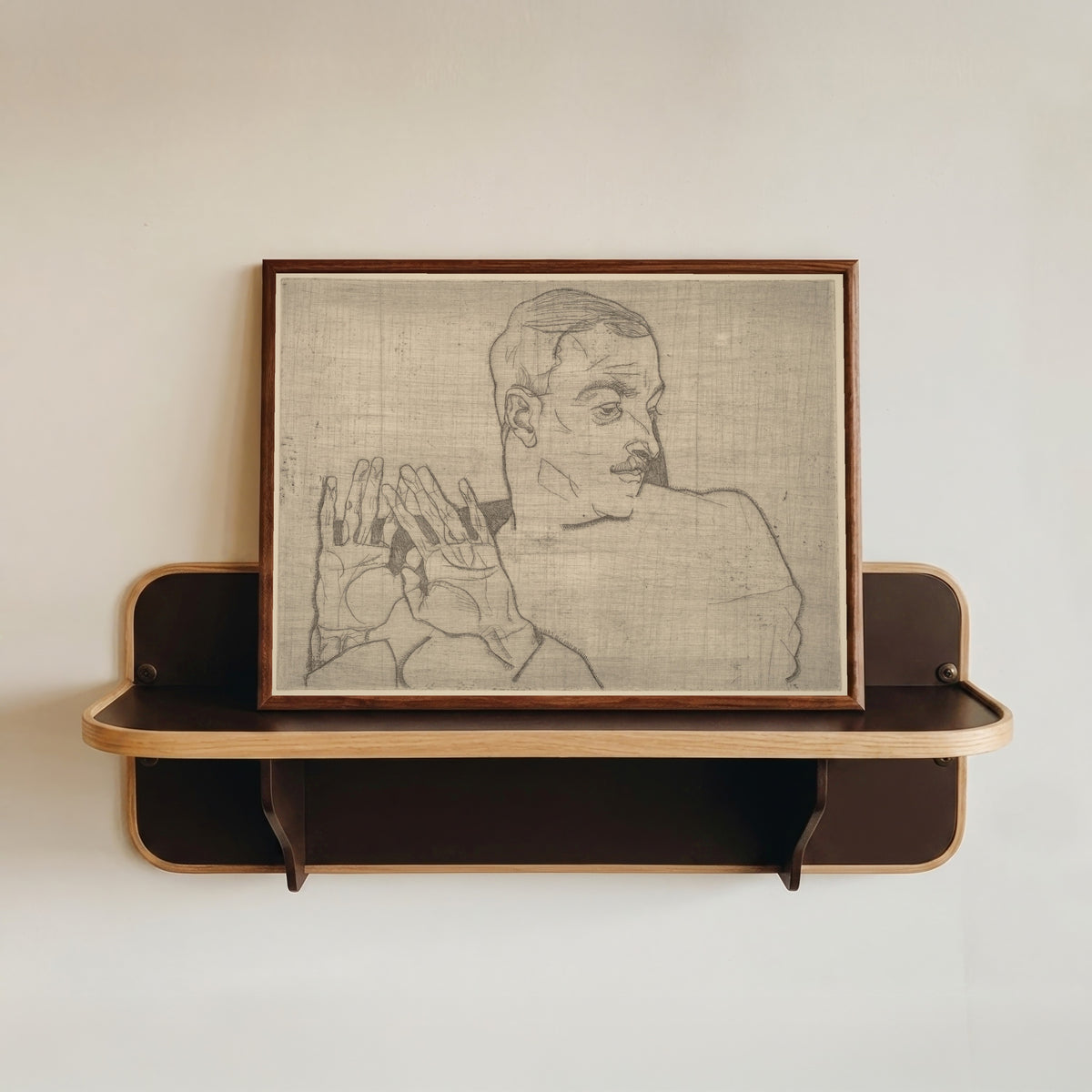 Framed art print of Portrait of Arthur Roessler by Egon Schiele, in a dark wood frame resting on a wall shelf