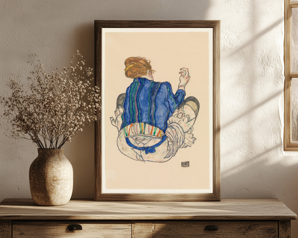 Framed art print of Seated Woman (blue jacket) by Egon Schiele, in a dark wood frame leaning on a rustic console beside dried flowers