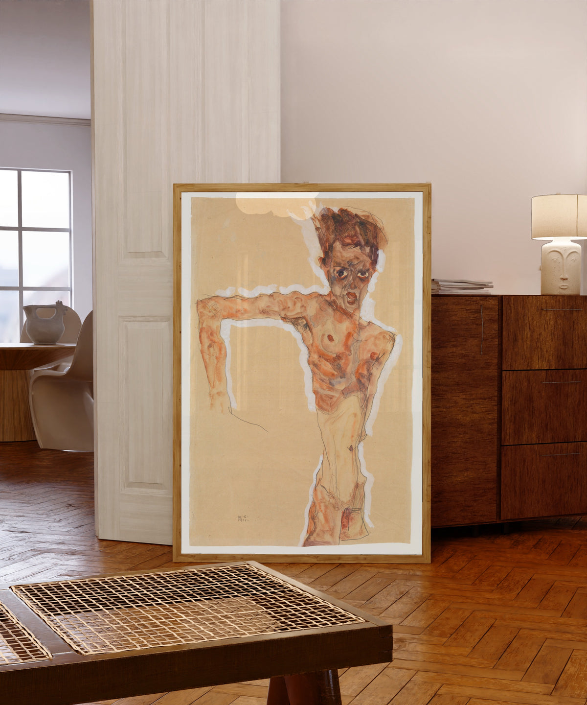 Framed art print of Self-Portrait by Egon Schiele, in a light wood frame leaning in a warm room with a parquet floor