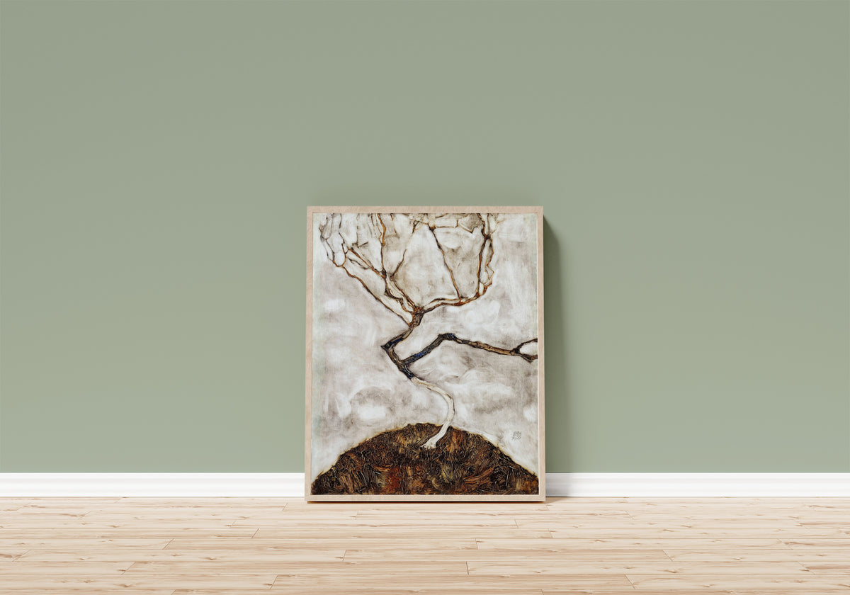 Framed art print of Small Tree in Late Autumn by Egon Schiele, in a light wood frame leaning on a sage green wall above a wooden floor