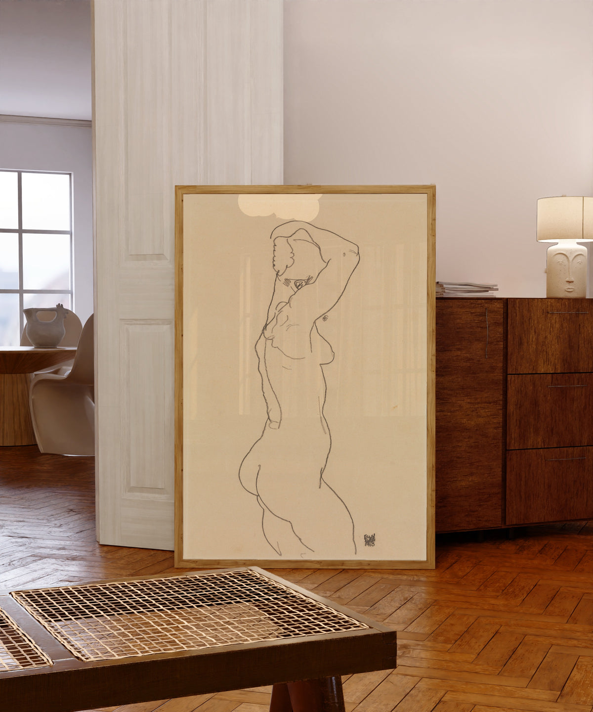 Framed art print of Standing Nude, Facing Right by Egon Schiele, in a light wood frame leaning in a warm room with a parquet floor