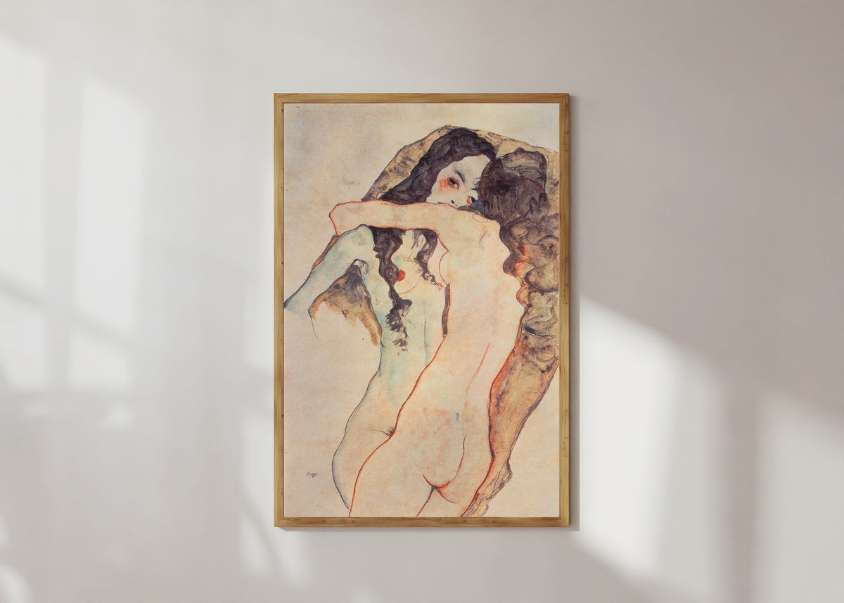 Framed art print of Two Embracing Women by Egon Schiele, in a light wood frame on a sunlit white wall