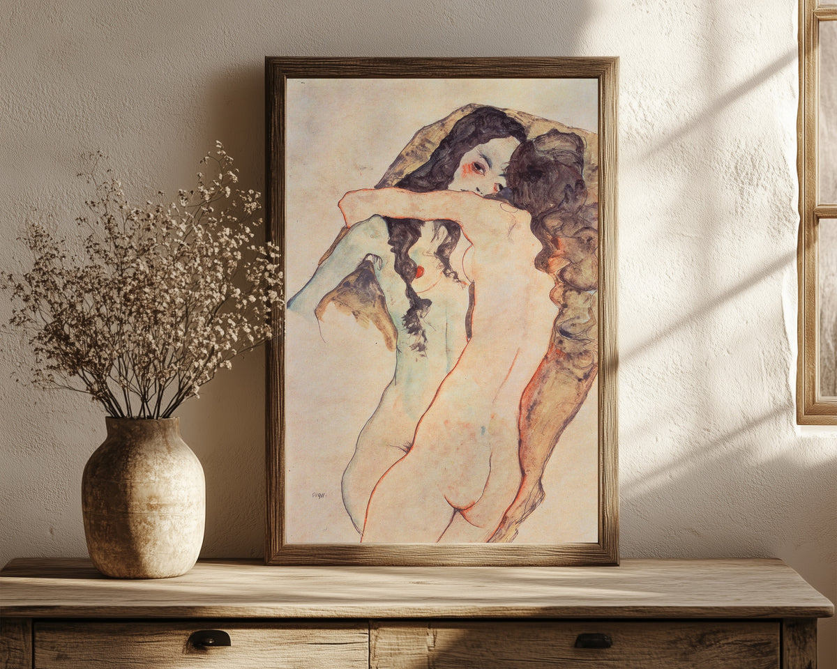 Framed art print of Two Embracing Women by Egon Schiele, in a dark wood frame leaning on a rustic console beside dried flowers