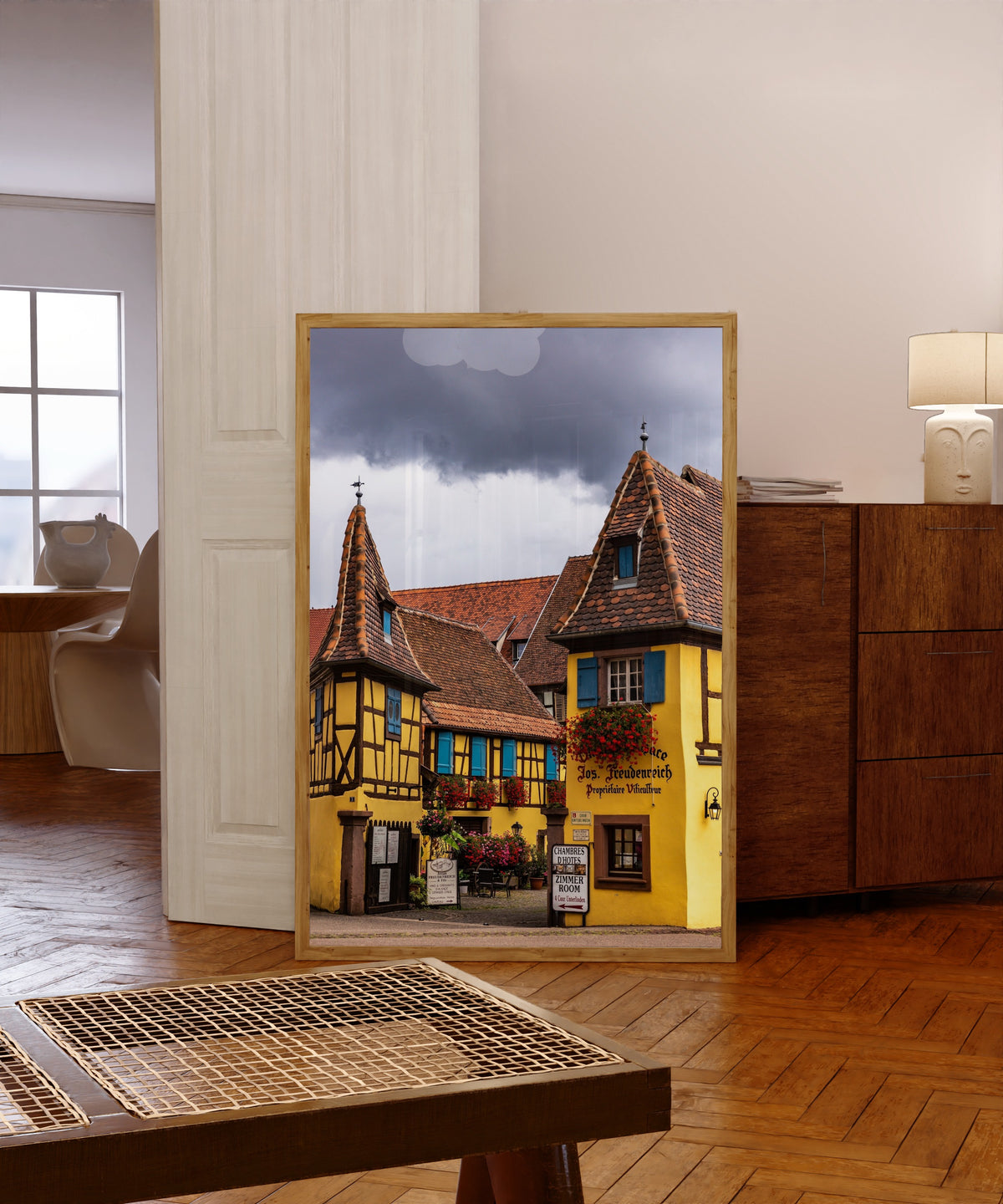 Framed art print of Eguisheim (Alsace) by Daniela Faust, in a light wood frame leaning in a warm room with a parquet floor