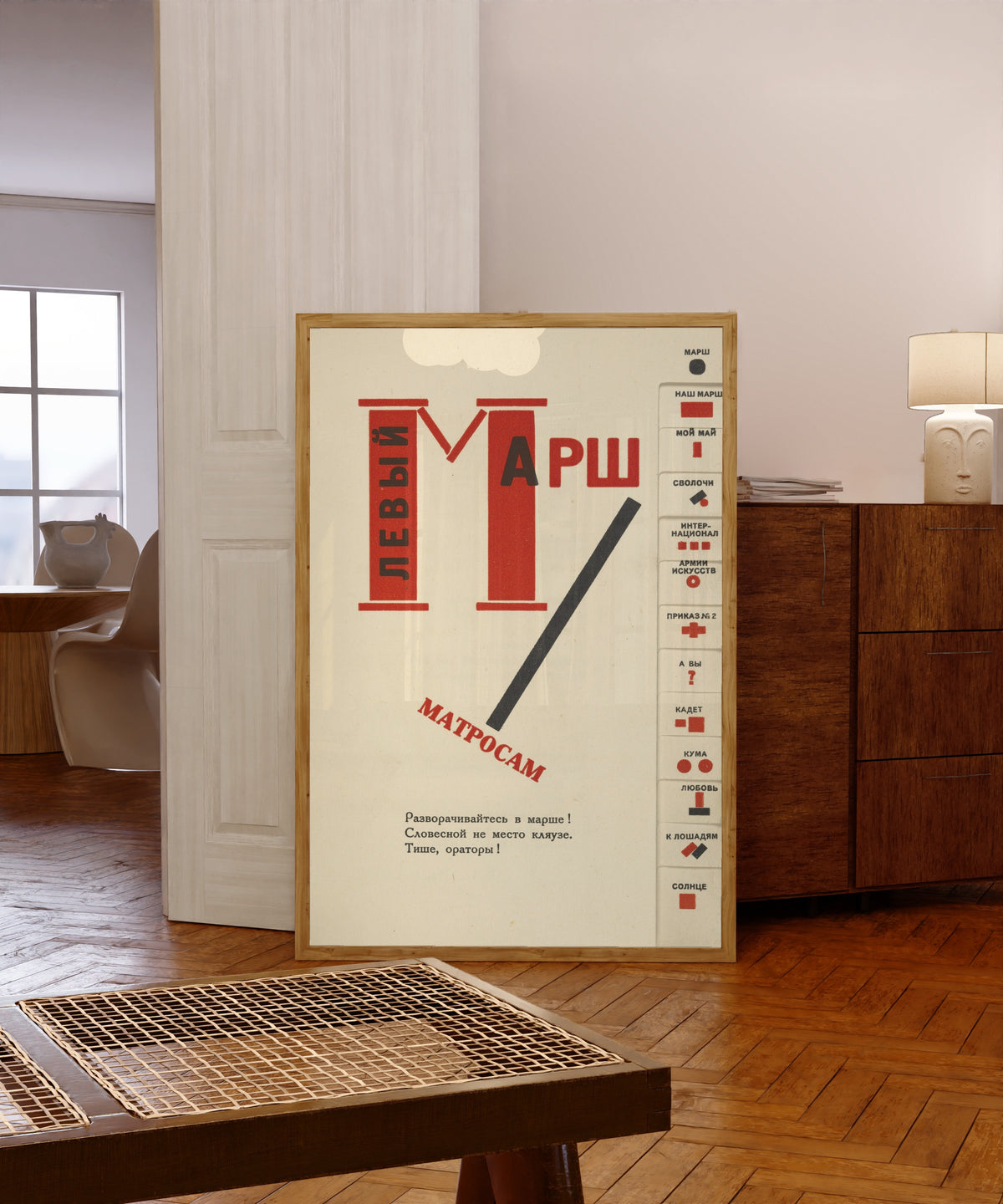 Framed art print of For the Voice: Left March (Title Page with Index Tabs) by El Lissitzky, in a light wood frame leaning in a warm room with a parquet floor