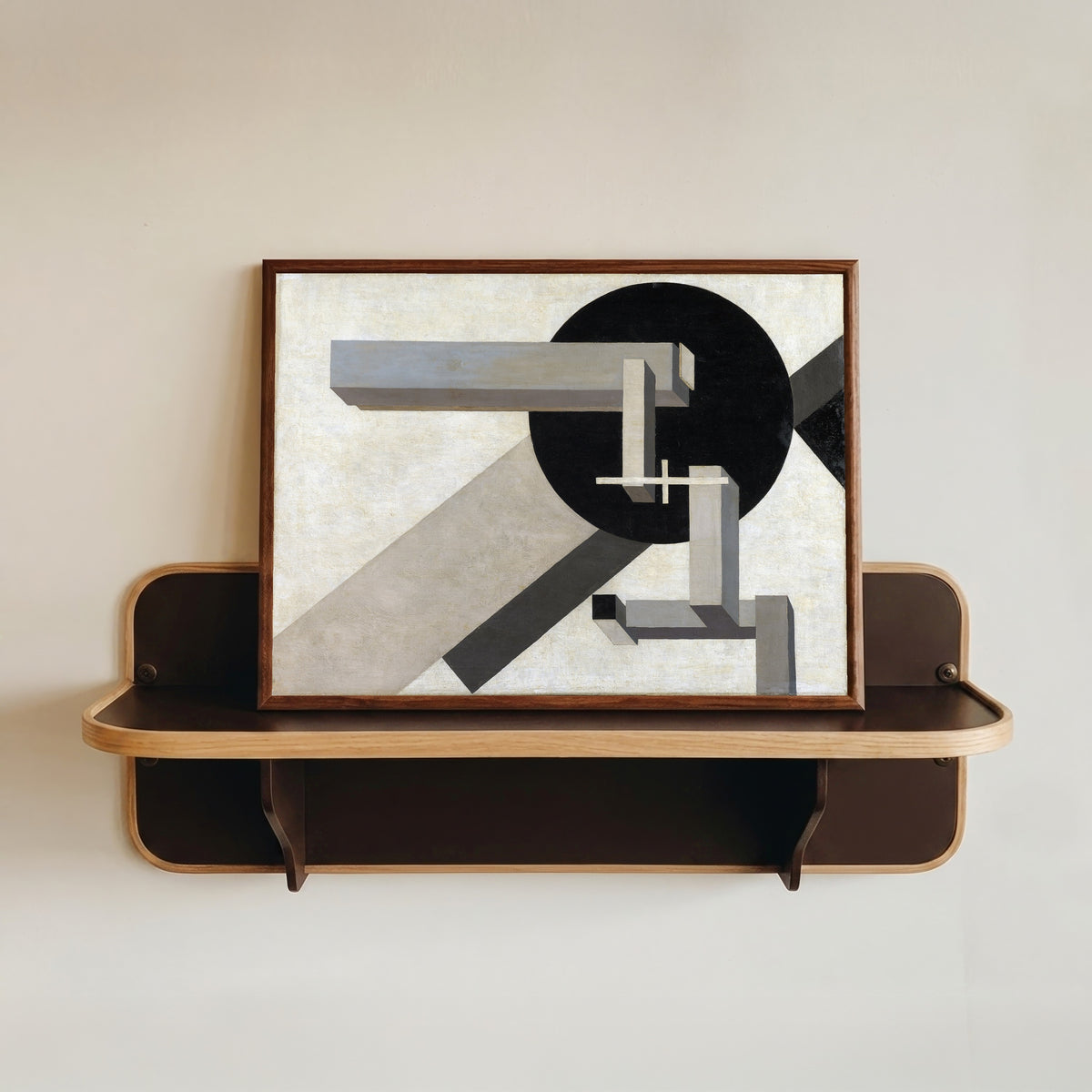 Framed art print of Proun 1D by El Lissitzky, in a dark wood frame resting on a wall shelf
