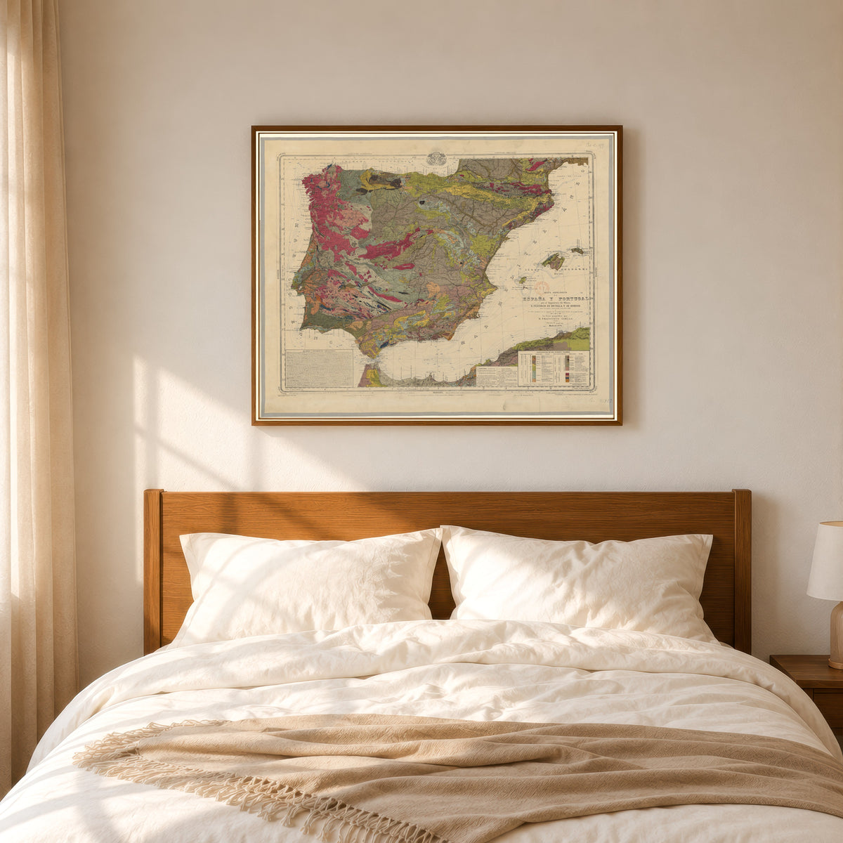 Framed art print of Mapa geológico de España y Portugal by Federico de Botella y de Hornos, in a slim wood frame above a bed in a sunlit bedroom