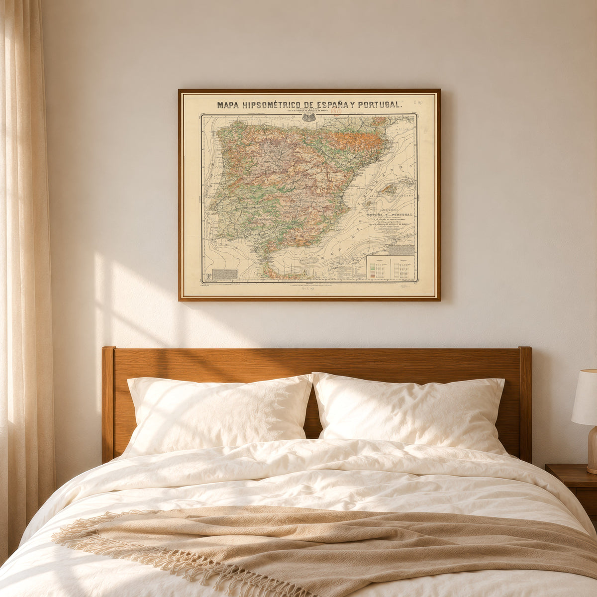 Framed art print of Mapa hipsométrico de España y Portugal by Federico de Botella y de Hornos, in a slim wood frame above a bed in a sunlit bedroom