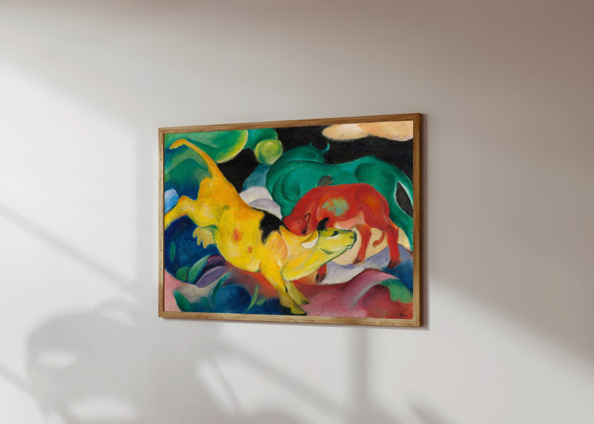 Framed art print of Cows, Red, Green, Yellow by Franz Marc, in a light wood frame on a sunlit white wall, seen at a slight angle