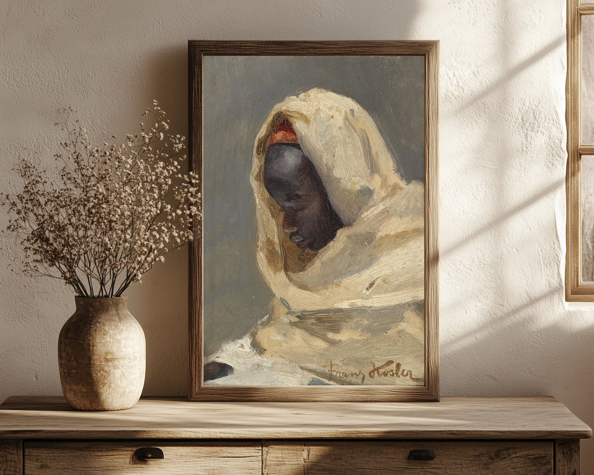 Framed art print of A Bedouin Man by Franz Xaver Kosler, in a dark wood frame leaning on a rustic console beside dried flowers