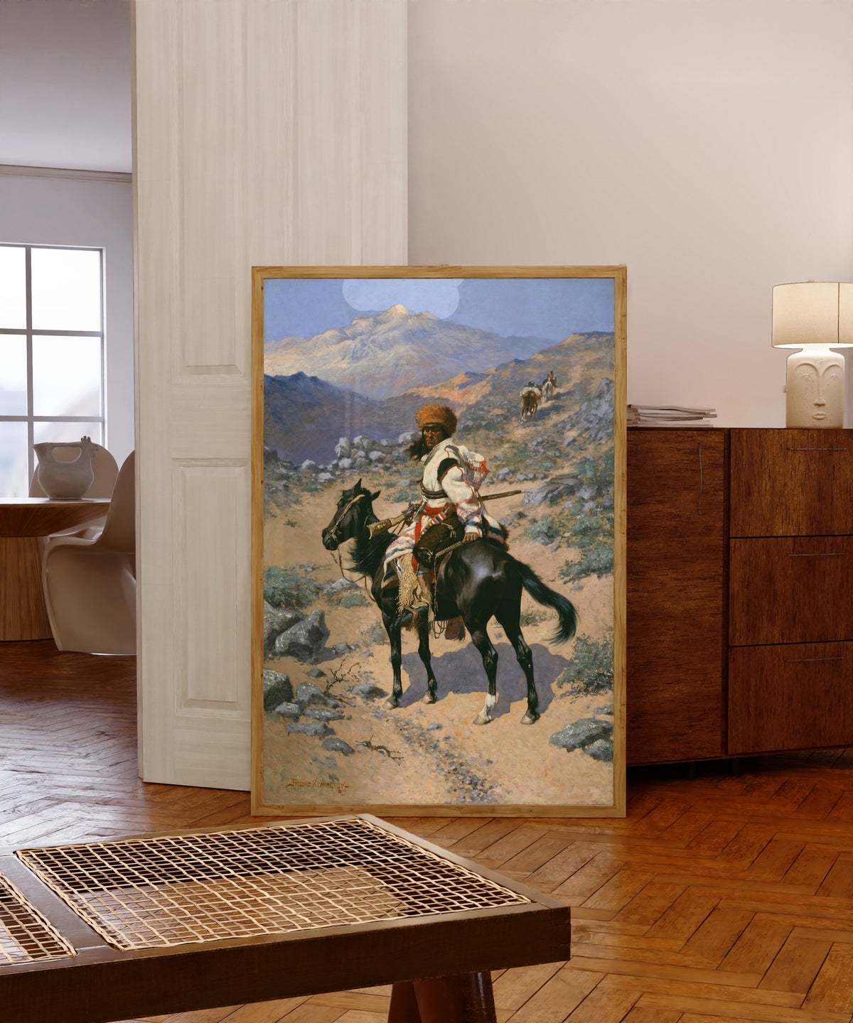 Framed art print of An Indian Trapper by Frederic Remington, in a light wood frame leaning in a warm room with a parquet floor