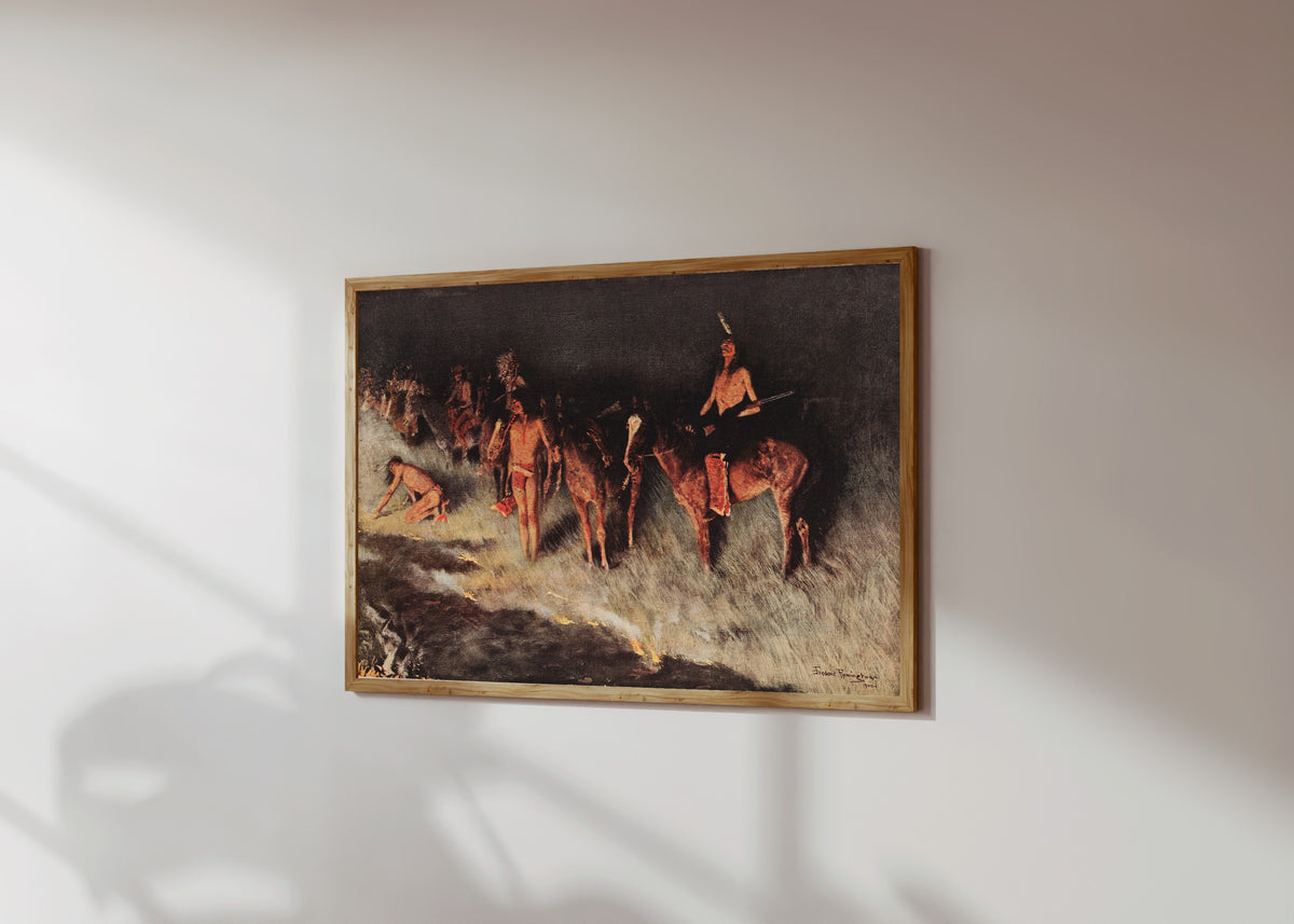 Framed art print of The Grass Fire by Frederic Remington, in a light wood frame on a sunlit white wall, seen at a slight angle