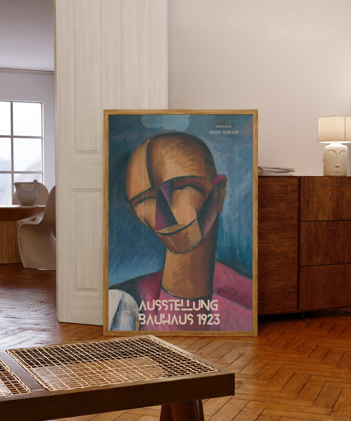 Framed art print of Hlava Muža by Gejza Schiller, in a light wood frame leaning in a warm room with a parquet floor