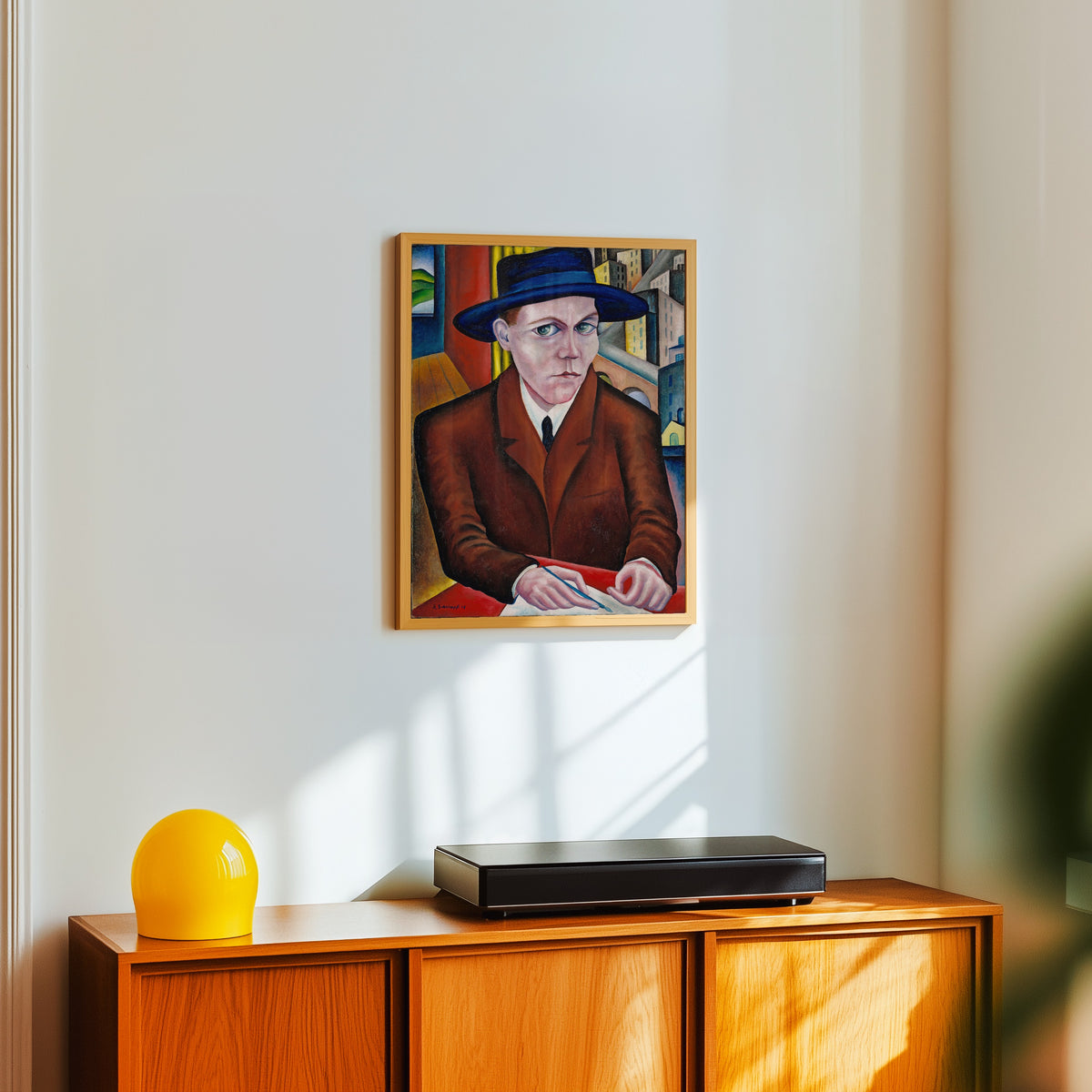 Framed art print of Oscar Maria Graf by Georg Schrimpf, in a light wood frame on a white wall above an orange sideboard