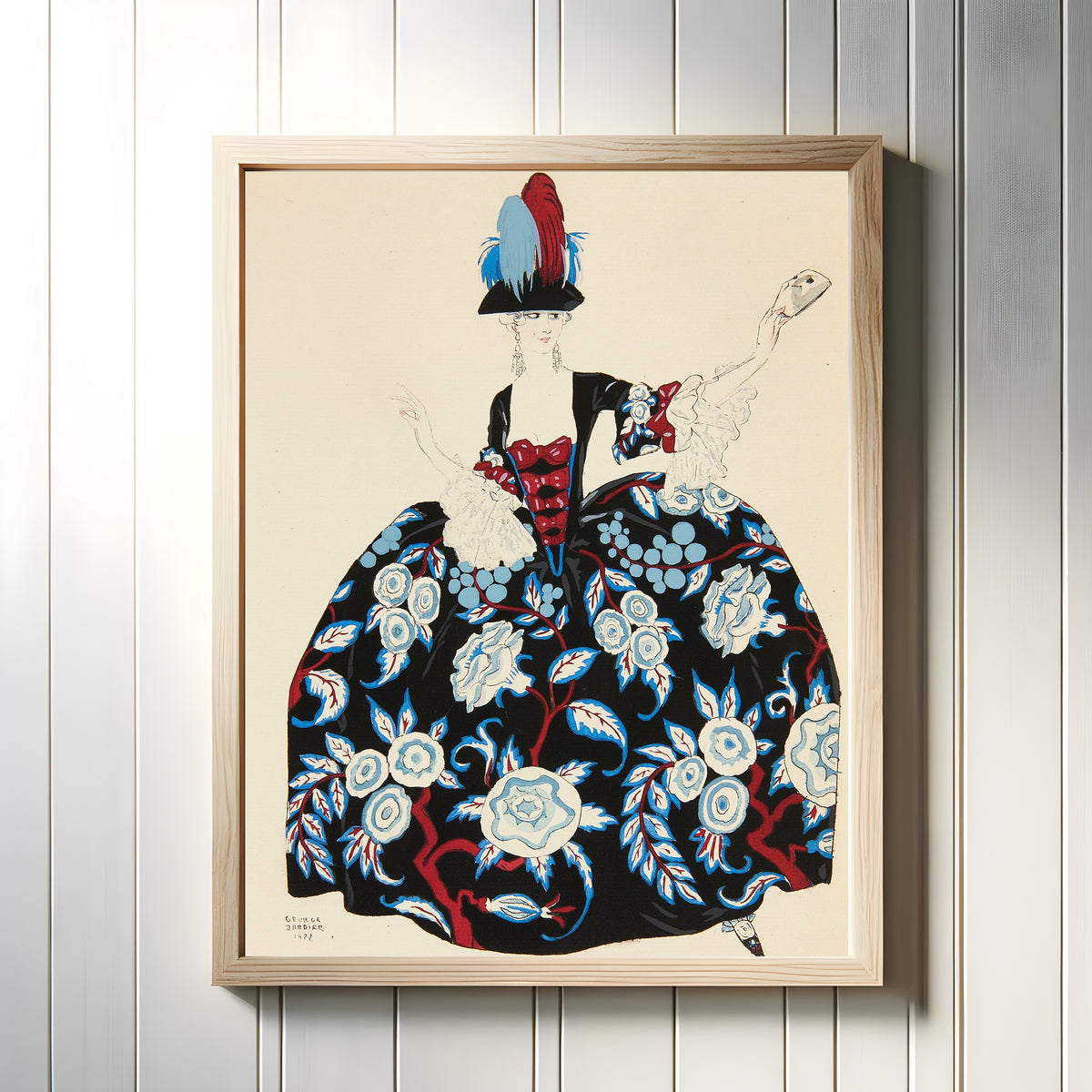 Framed art print of Costumes for theater (Lady with a Mask) by George Barbier, in a light wood frame on a white panelled wall