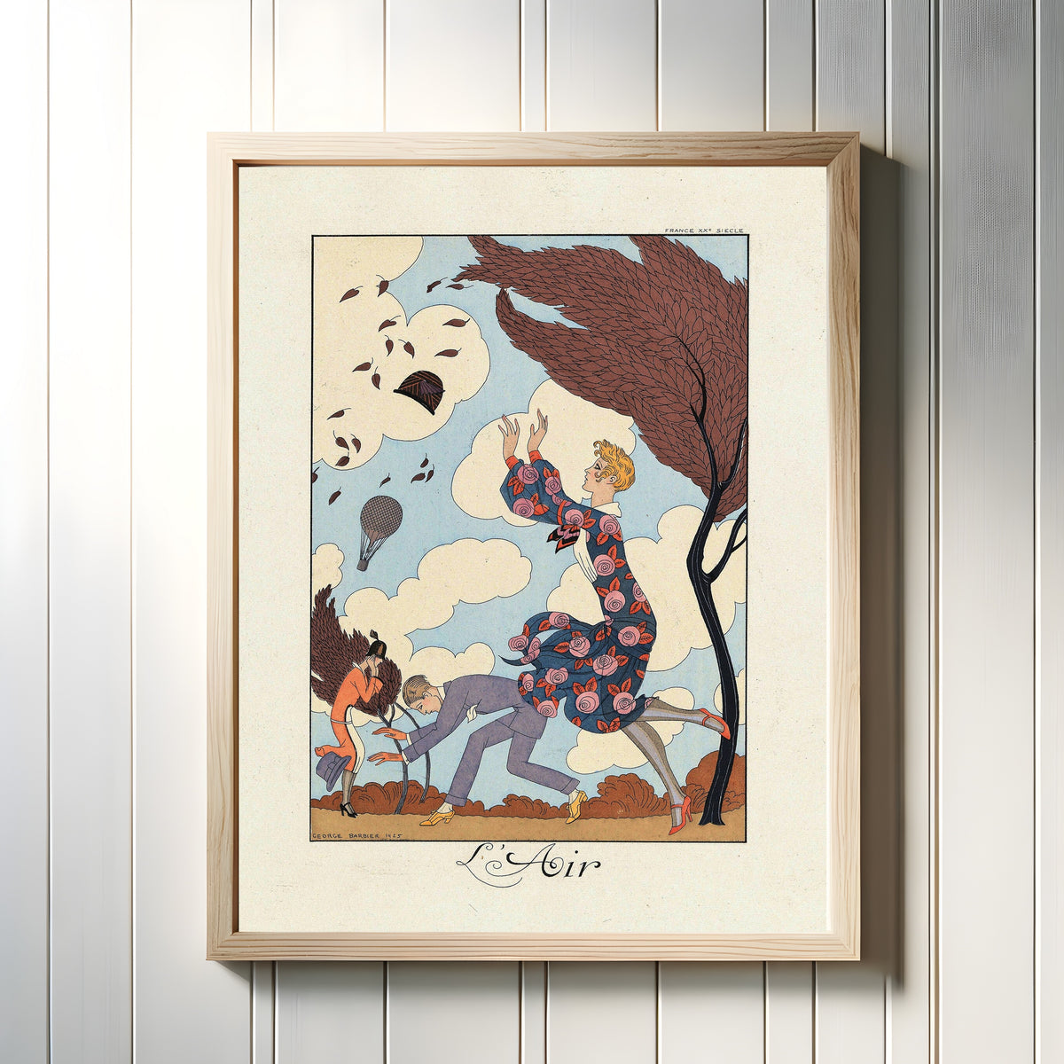 Framed art print of L'Air by George Barbier, in a light wood frame on a white panelled wall